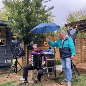 Michel protège de son parapluie l'accordéon de Pamphile pendant le concert au Baracrep.